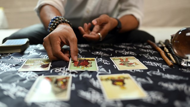 A fortune teller arranges tarot cards on table.